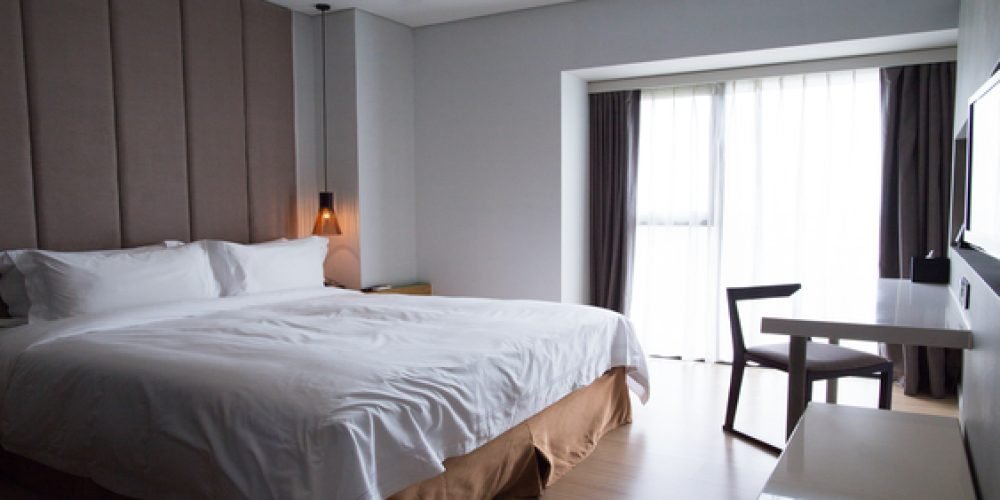 Comfortable hotel bedroom interior with double bed, table, chair and TV set