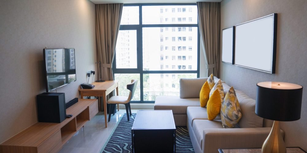 Cozy living room interior design with panoramic window. White sofa with colorful pillows and coffee table placed opposite TV. Apartment and interior concept