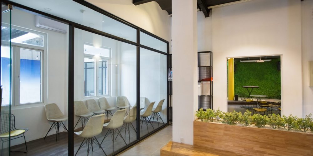 Nobody in office lobby with wooden bench. White wall with column and shelves. Green plants as part of interior. Many chairs behind glassy wall. Business center concept